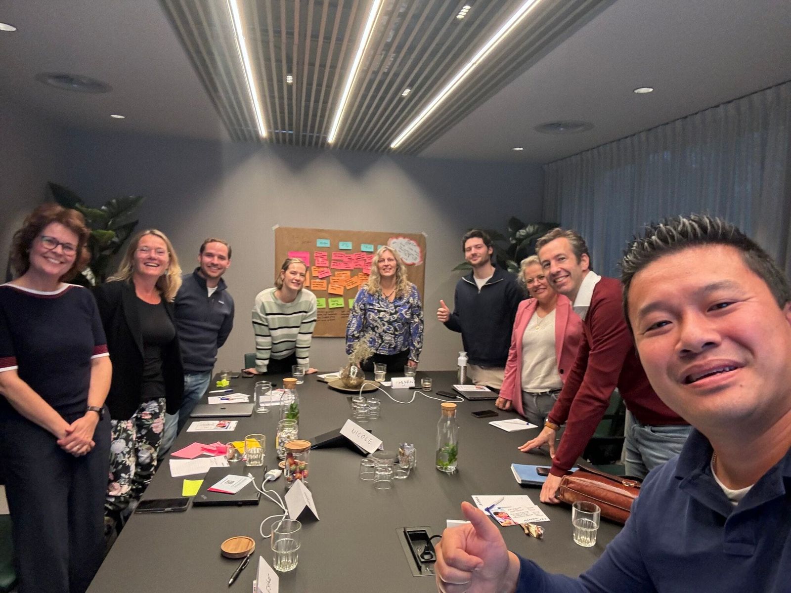 Deelnemers van een workshop rond een tafel, met post-its op de wand erachter