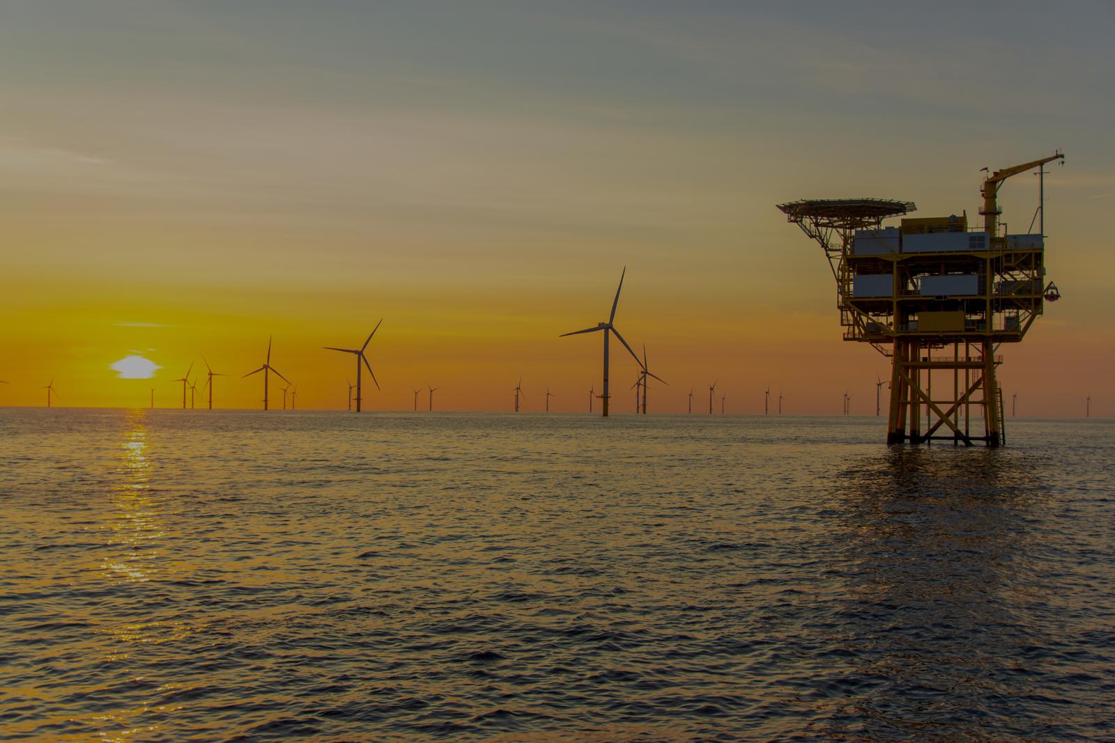 Een offshoreplatform in zee bij zonsondergang, met een windpark aan de horizon