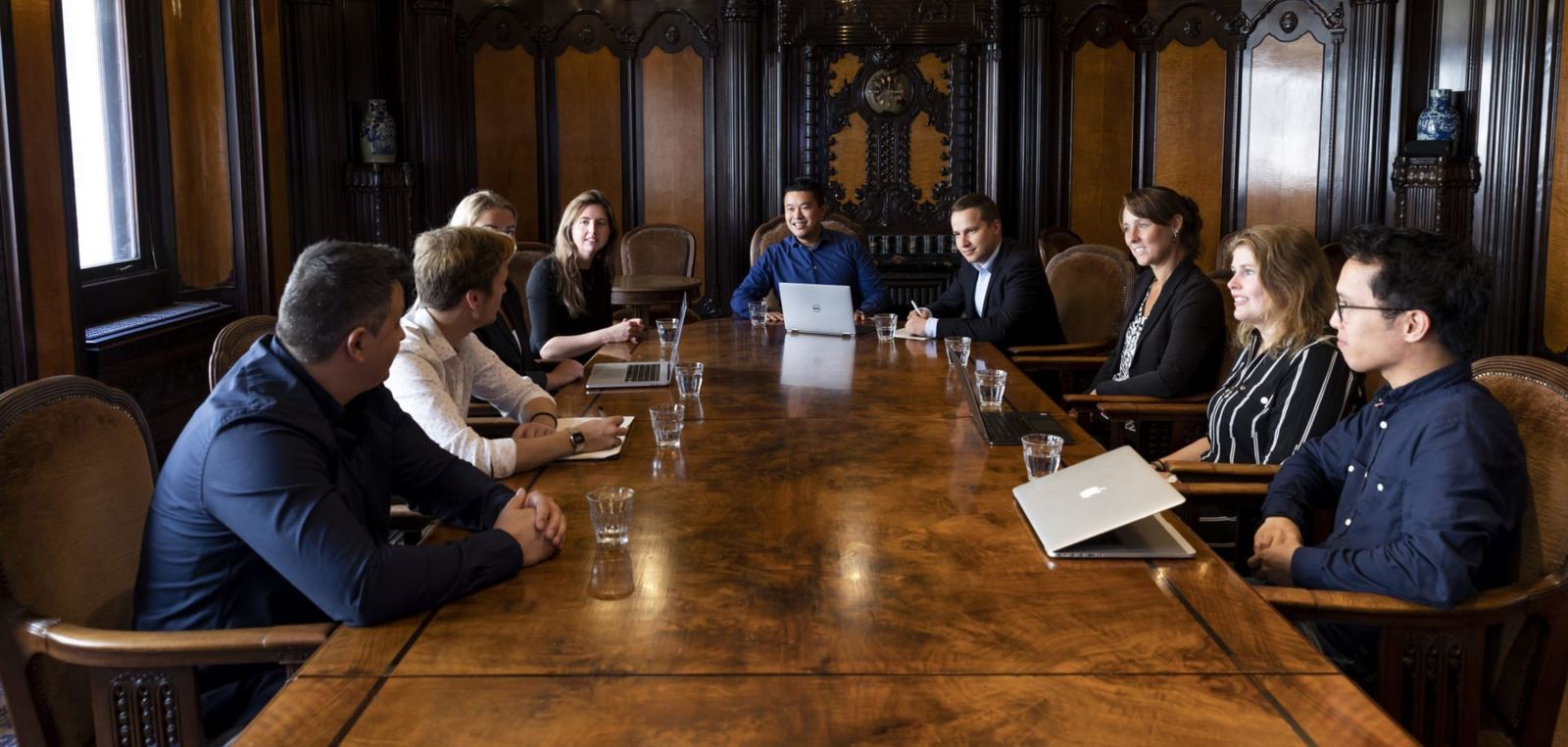 Het team van Synerflow rond een lange vergadertafel in een betimmerde zaal
